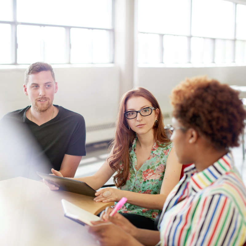Unposed multi-cultural group of business people in an open concept office sitting at a table being coached