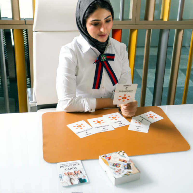 Muslim woman sitting at an office desk holding and reading a set of resilience cards