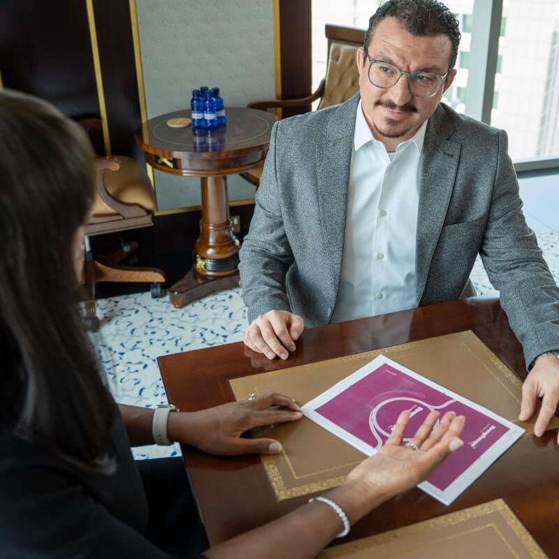 Handsome young executive in a one to one leadership coaching session holding a brochure and listening to a woman sitting opposite him